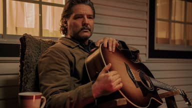 Pedro Pascal as Joel in The Last of Us. He is holding a guitar on his porch