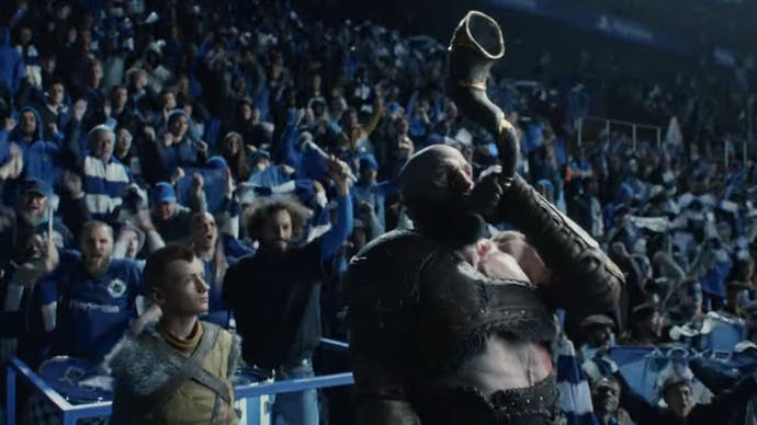 Kratos toots the Gjallarhorn in a crowd at a football game, while his son Atreus stands to his side.
