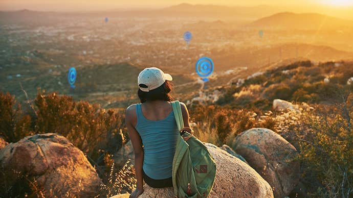 Real person sitting on a rocky hillside staring at virtual PokeStops in the distance.
