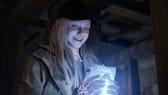 Rose smiles while clutching a glowing item in Resident Evil Village DLC, Shadows of Rose.
