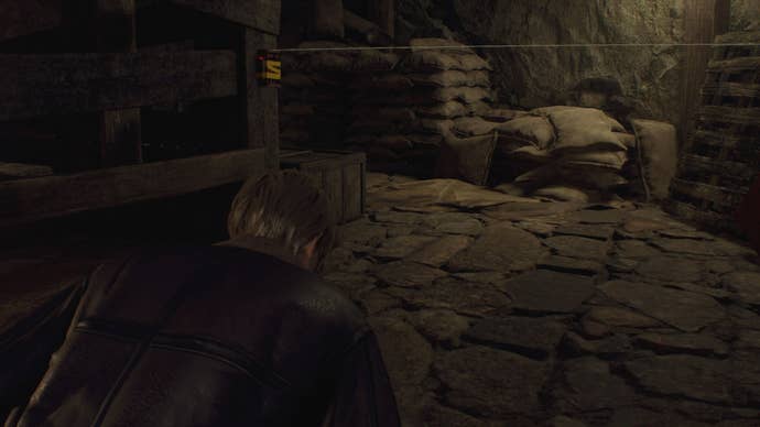 Leon crouches beneath a tripwire in Chapter 1 of the Resident Evil 4 remake