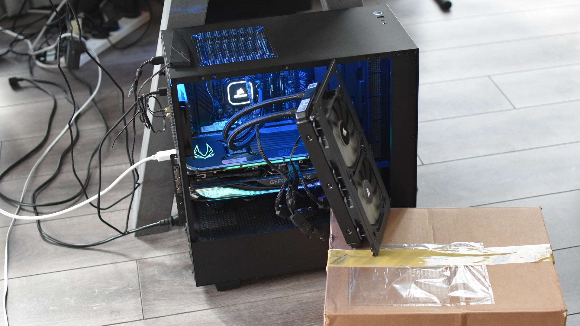 An RTX 4090 graphics cards running inside a PC, with the AIO cooler&rsquo;s radiator and fans forced outside of the case due to the GPU being so damn big.