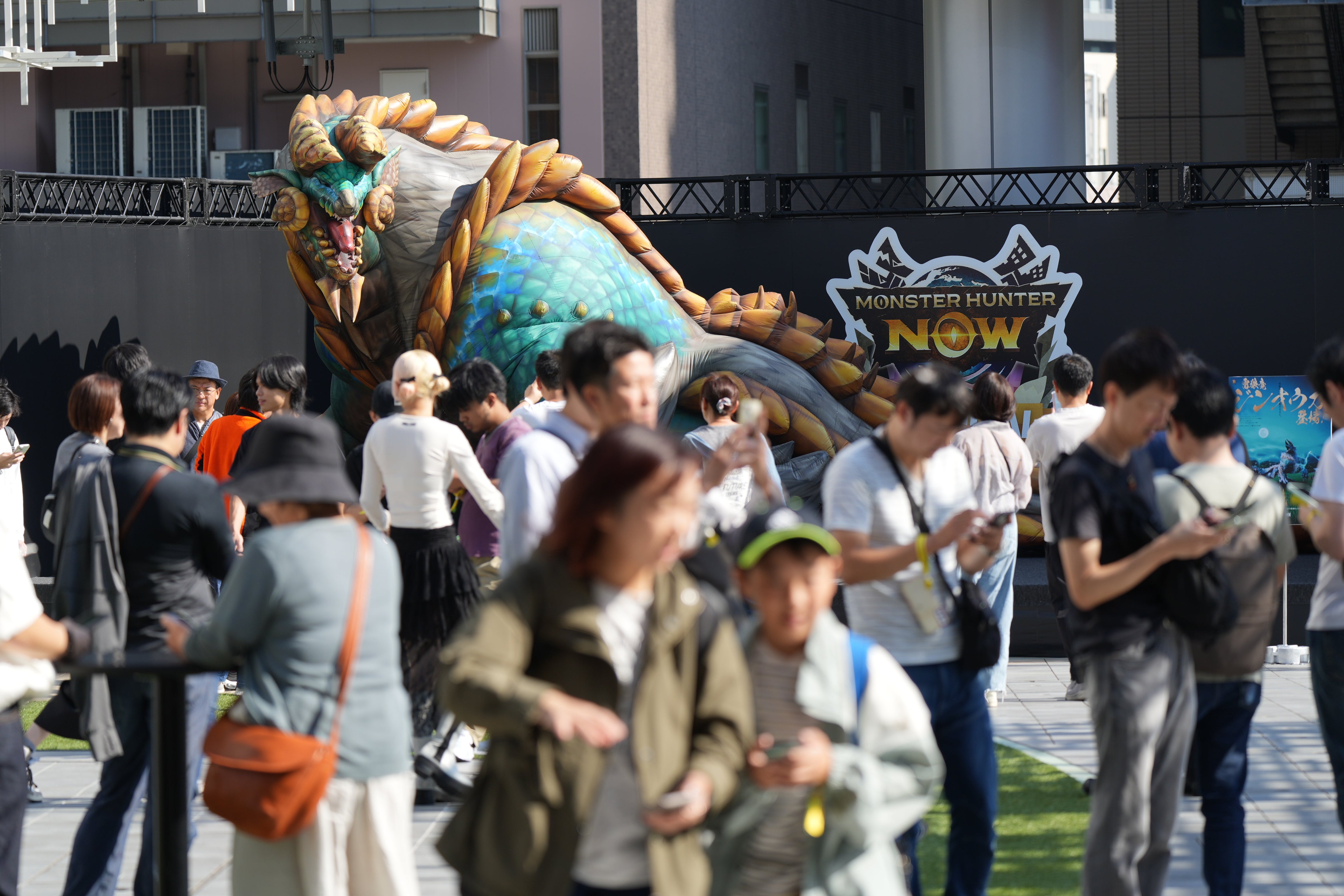 A giant Zinogre stands in the background of a bunch of people playing Monster Hunter Now in Tokyo.