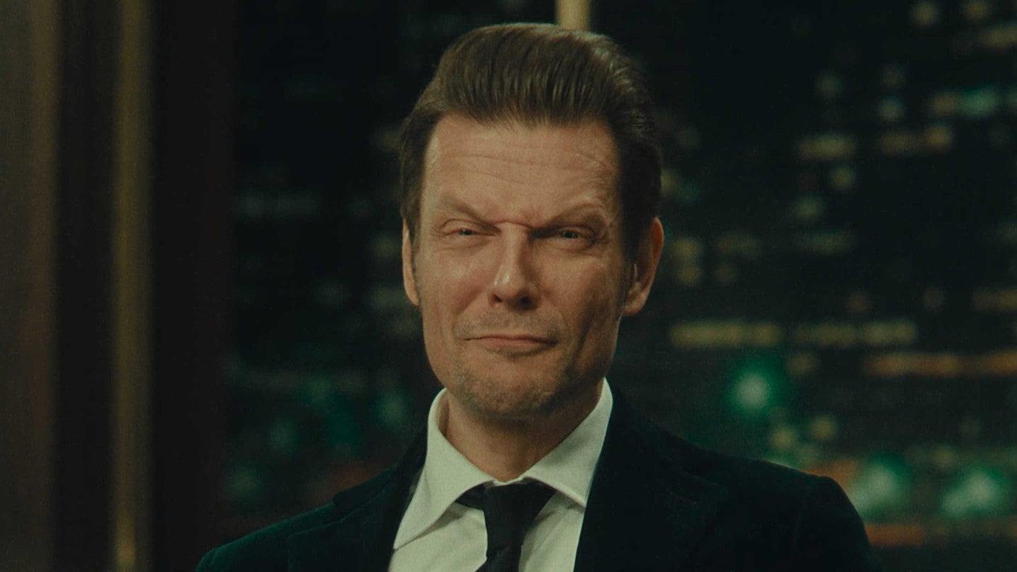 Sam Lake in Alan Wake 2, wearing a suit and tie while pulling funny faces at the camera