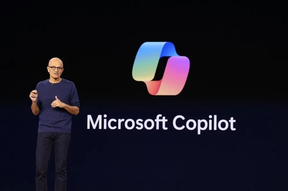 Microsoft's Satya Nadella on stage against a black background and the logo for Microsoft Copilot