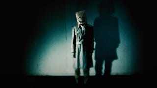 Who is Emio teaser showing a man wearing a paper bag with a smile drawn on it.