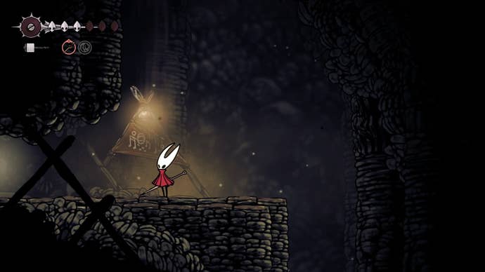 Hornet stands by an illuminated sign in Blasted Steps in Hollow Knight: Silksong