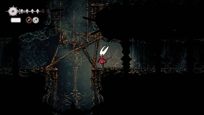 Hornet stands beside a breakable wooden barricade in the Exhaust Organ in Hollow Knight: Silksong