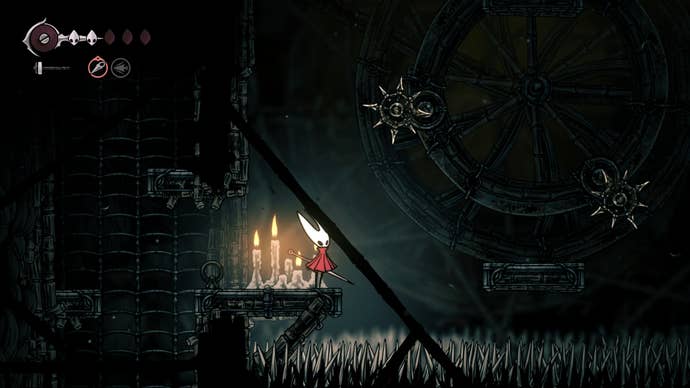 Hornet stands behind a wheel with multiple spiked wheel traps on it in Greymoor in Hollow Knight: Silksong