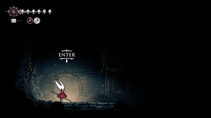 Hornet stands in front of a cave entrance in The Slab in Hollow Knight: Silksong