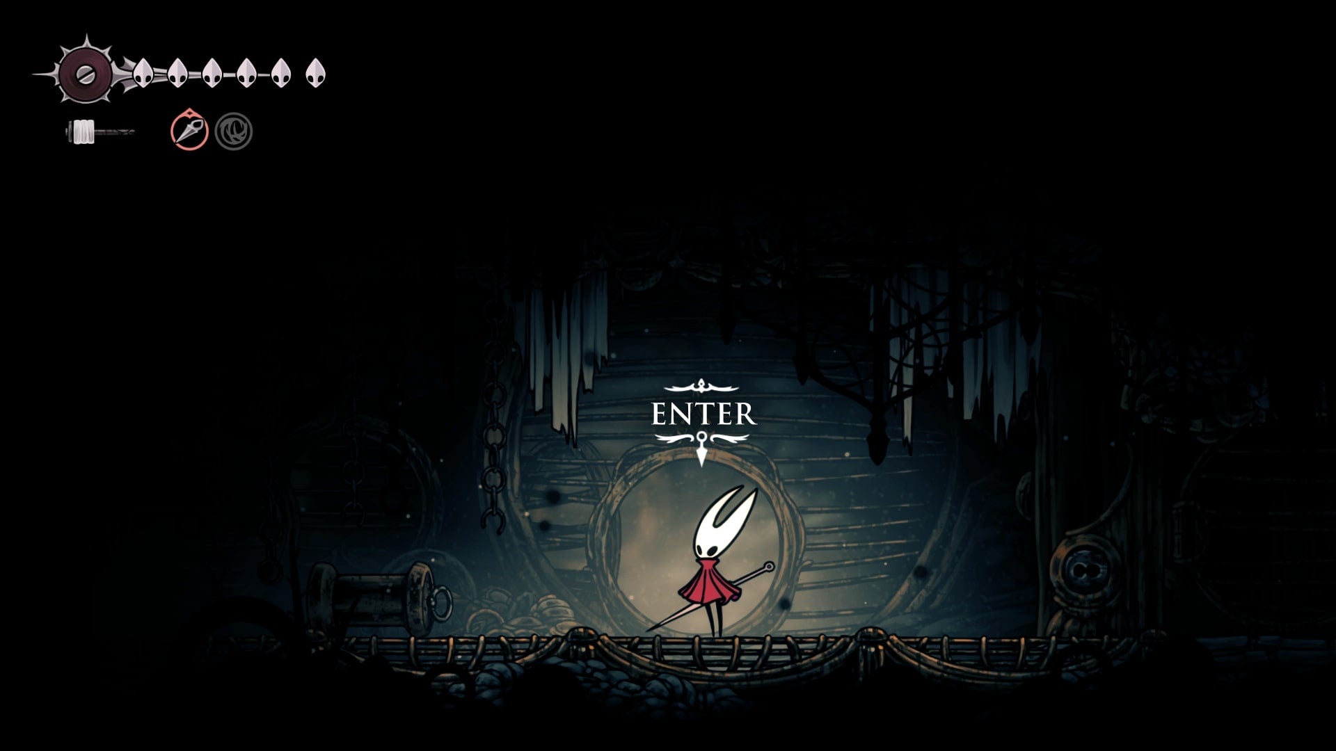 Hornet stands in front of a cave entrance in The Slab in Hollow Knight: Silksong