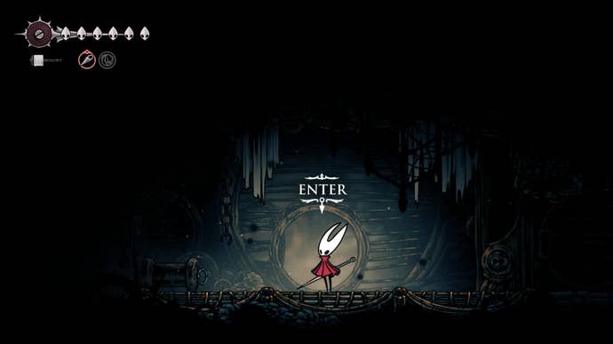 Hornet stands in front of a cave entrance in The Slab in Hollow Knight: Silksong