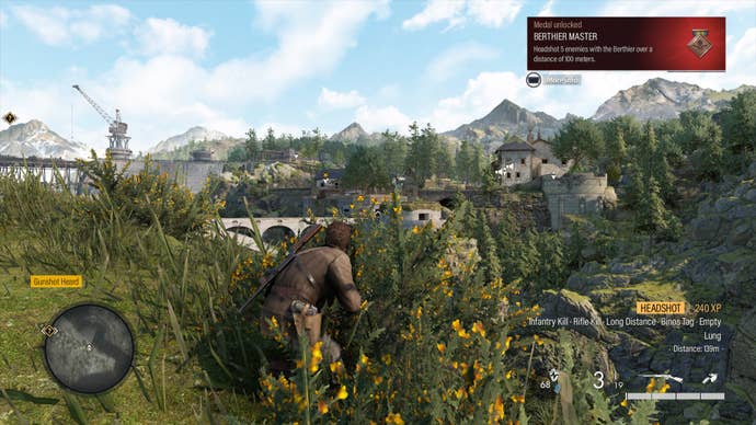 Harry crouches in the undergrowth on a sunny day in Sniper Elite Resistance. In the distance is a French chateau and a dam. In the top corner, Harry has secured a medal for “Berthier Master” whilst the bottom-right explains there has just been a headshot at 139m. The bottom left shows the gunshot was heard.