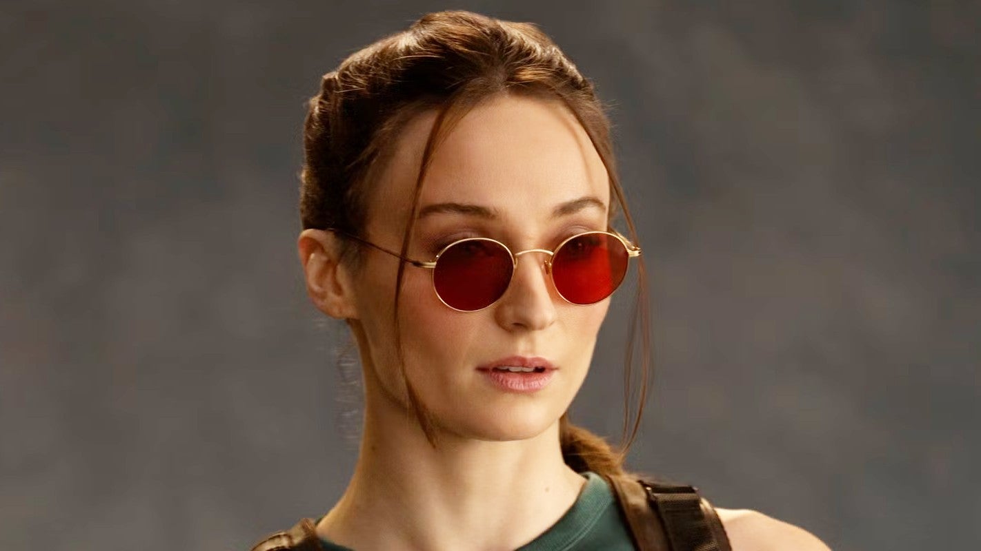 Sophie Turner as Lara Croft. She has red glasses on, and her hair is tied back from her face
