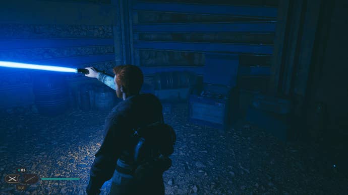 Star Wars Jedi Survivor screenshot showing Cal holding up a lightsaber to illuminate a chest in a dark cave.