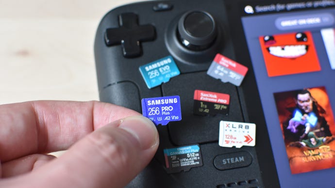 A Steam Deck microSD card is held up in front of several others, which are laying on a Steam Deck OLED.