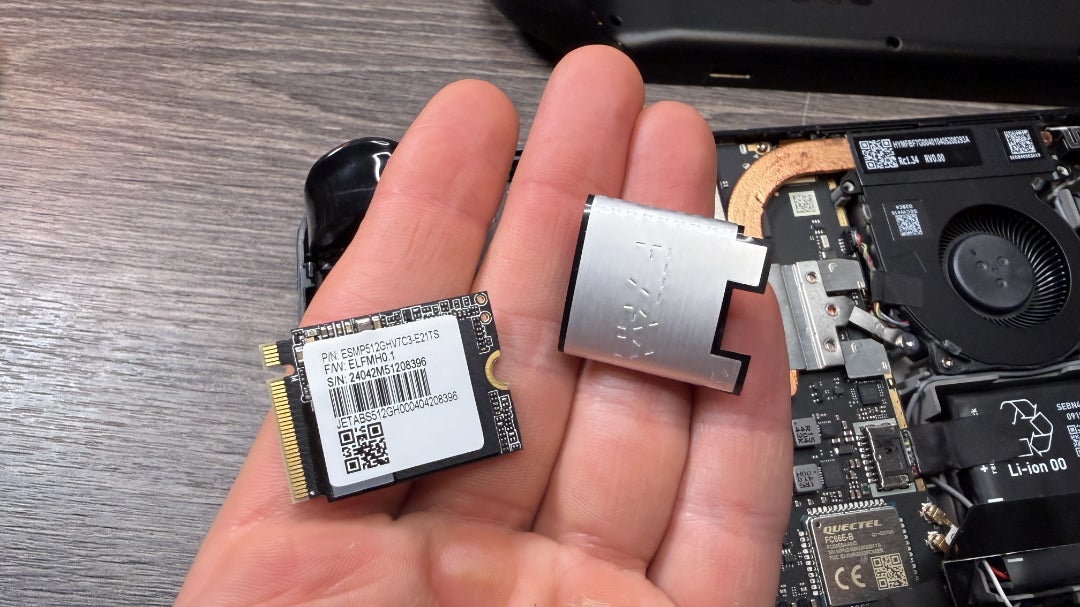 The stock Steam Deck OLED SSD, being held in a hend along with its protective cover.