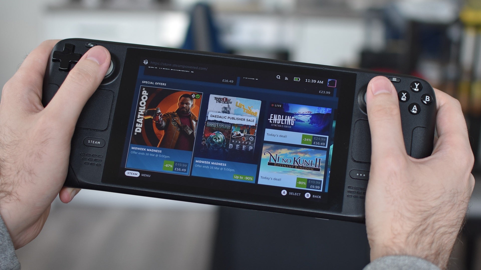 The Steam Deck behind held in two hands, showing the Steam store&rsquo;s sales section.