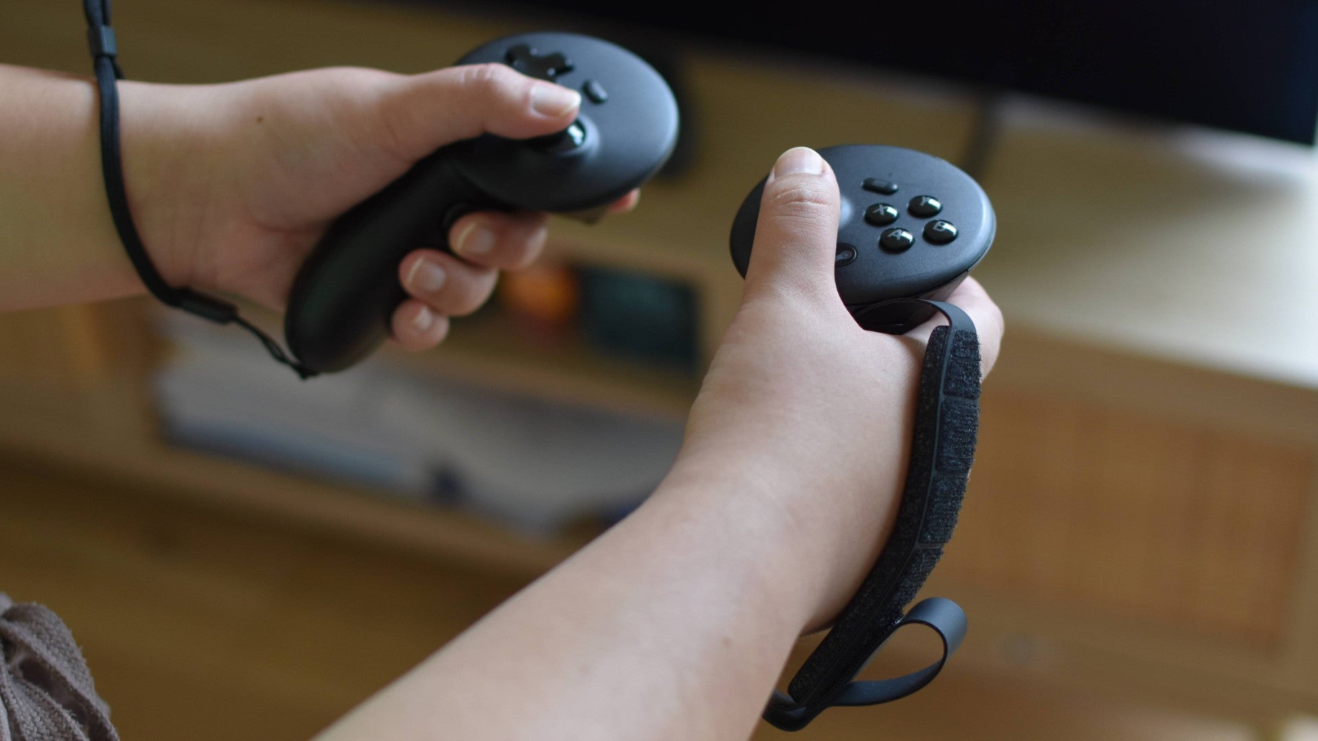 A pair of hands holding the Steam Frame controllers. One is using the default strap, the other is using the optional Ergonomic Accessories Pack strap.