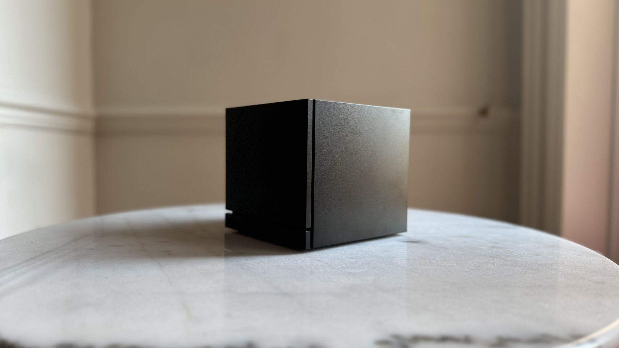 Steam Machine photograph showing the steam machine with black faceplate on a marble circular table in front of a grey/beige wall, from a diagonal angle