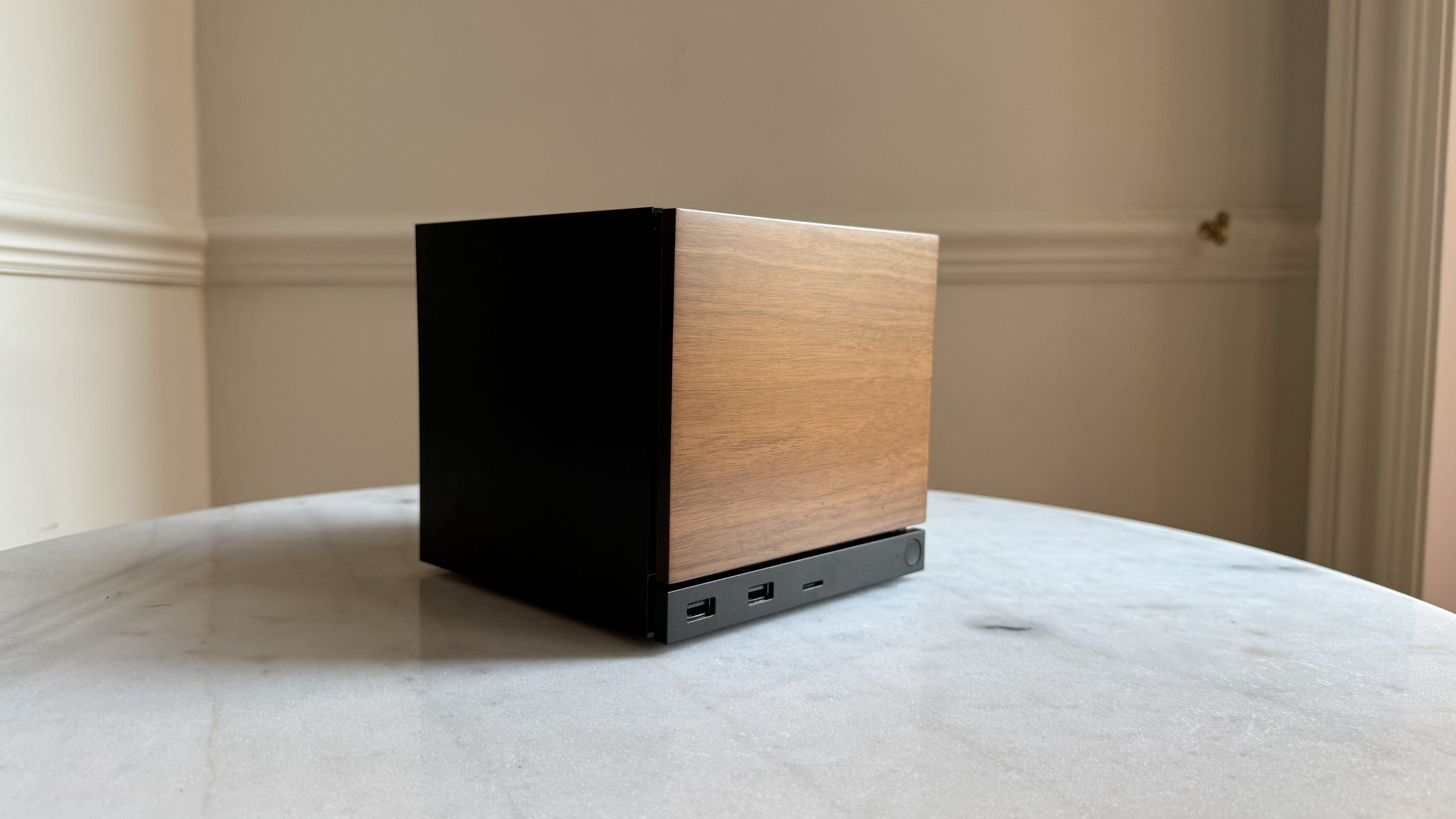 Steam Machine photograph showing the steam machine with wood faceplate on a marble circular table in front of a grey/beige wall, from diagonal angle