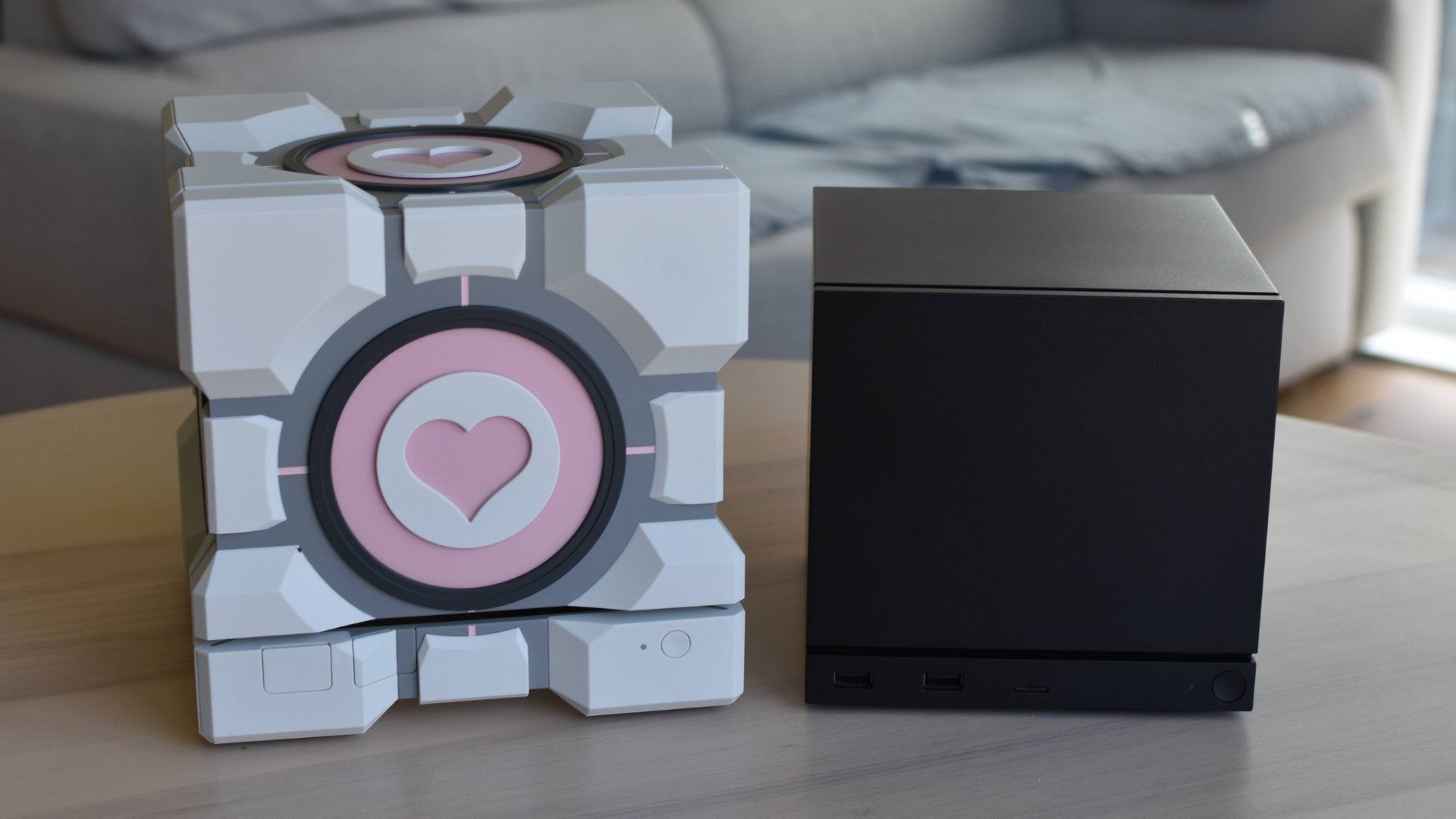 A Steam Machine on a table next to Dbrand's Companion Cube case, show how much bigger the case is.