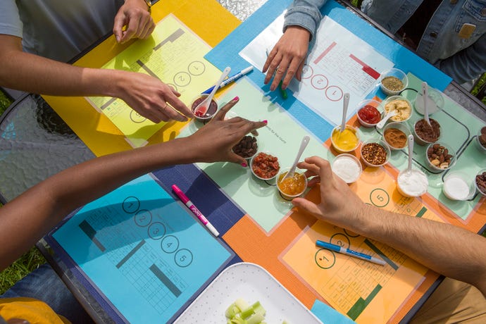 Several people playing a game about tasting food using pen and coloured card