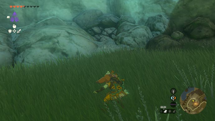 Link crouching in a grassy area near a cave entrance that has been covered in debris.