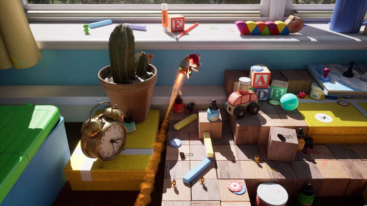 Plucky Squire screenshot showing the cartoonish Squire with a smiling rocket backpack flying over a desk covered in toys and building blocks, with an old alarm clock and a cactus on the side
