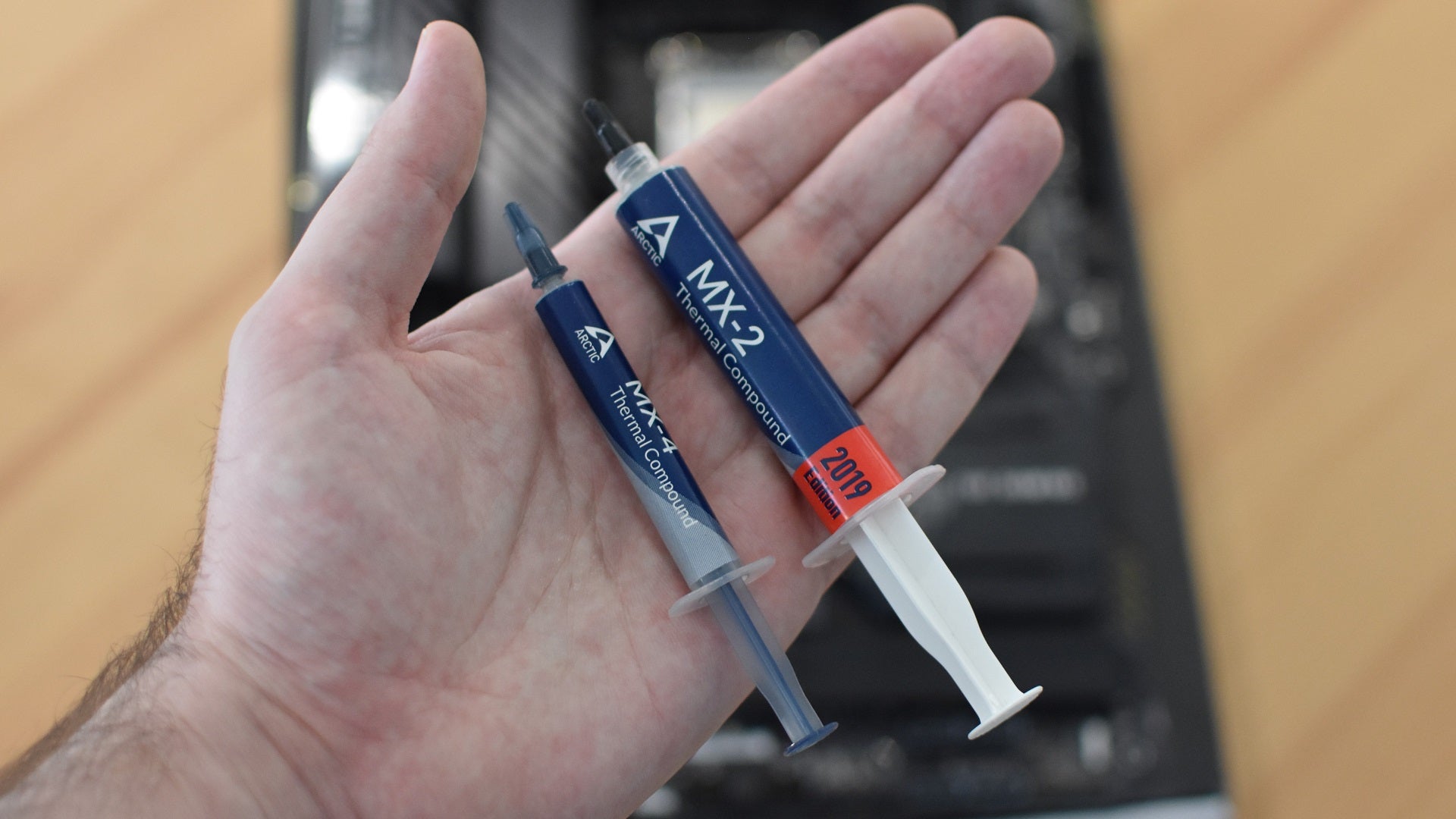 A small tube of thermal paste, held in a hand over a PC build in progress.