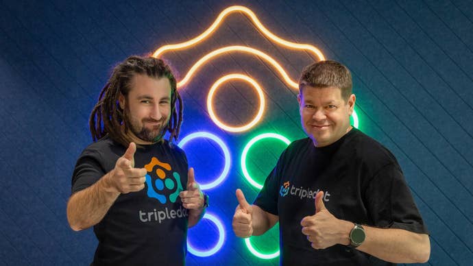 двое мужчин стоят перед неоновой вывеской с логотипом Tripledot