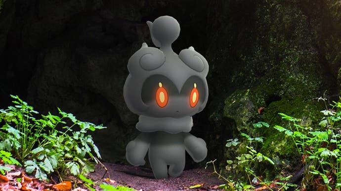Mythical ghostly Pokémon Marshadow, a small black smoky figure with red eyes, looks out of a cave.