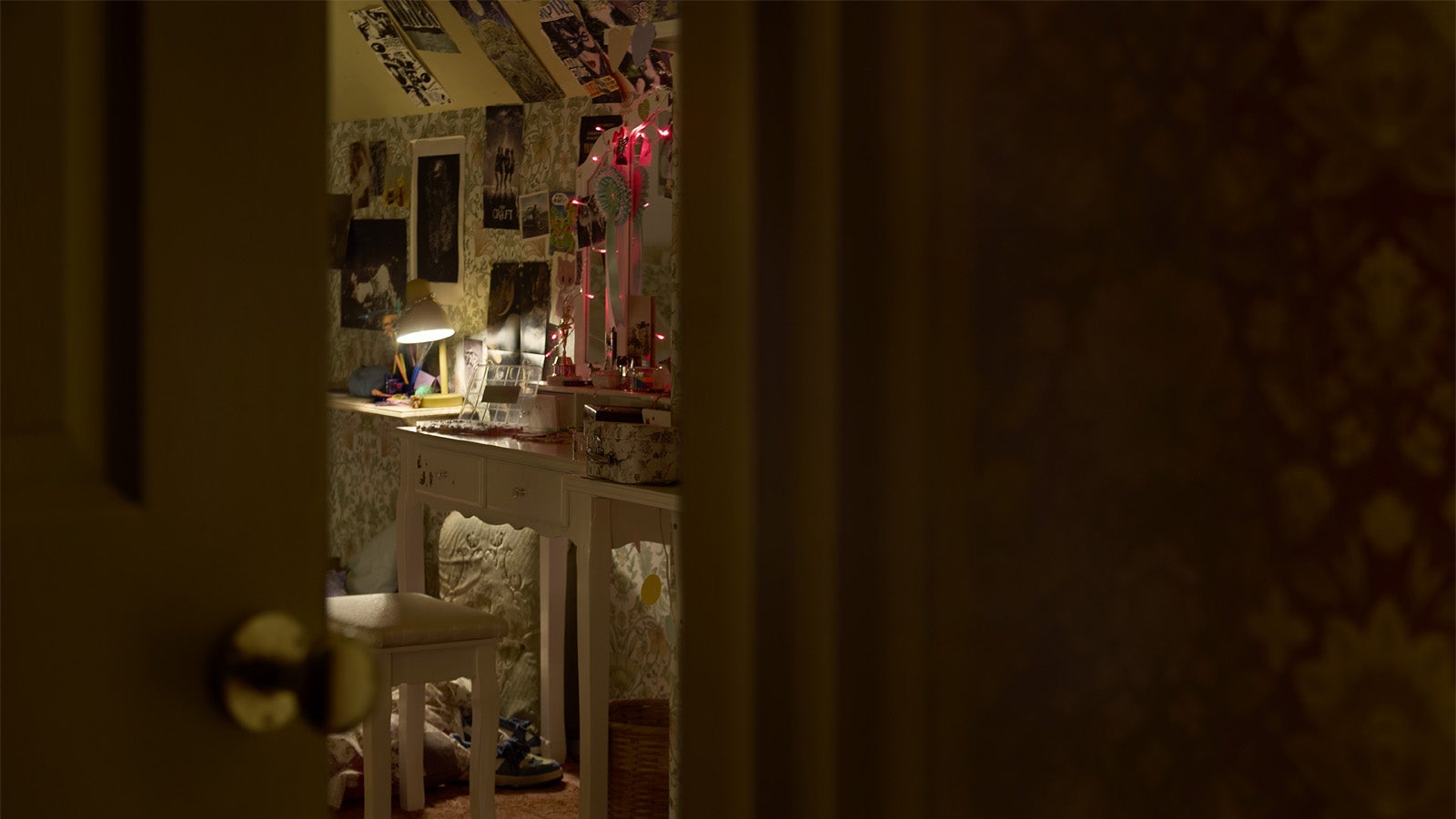 Photograph showing a look into Viola&rsquo;s bedroom, a typical teenage room with posters on the ceiling and walls, a messy table and low lighting.