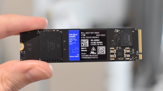 A WD Blue SN580 SSD being held between a finger and thumb.
