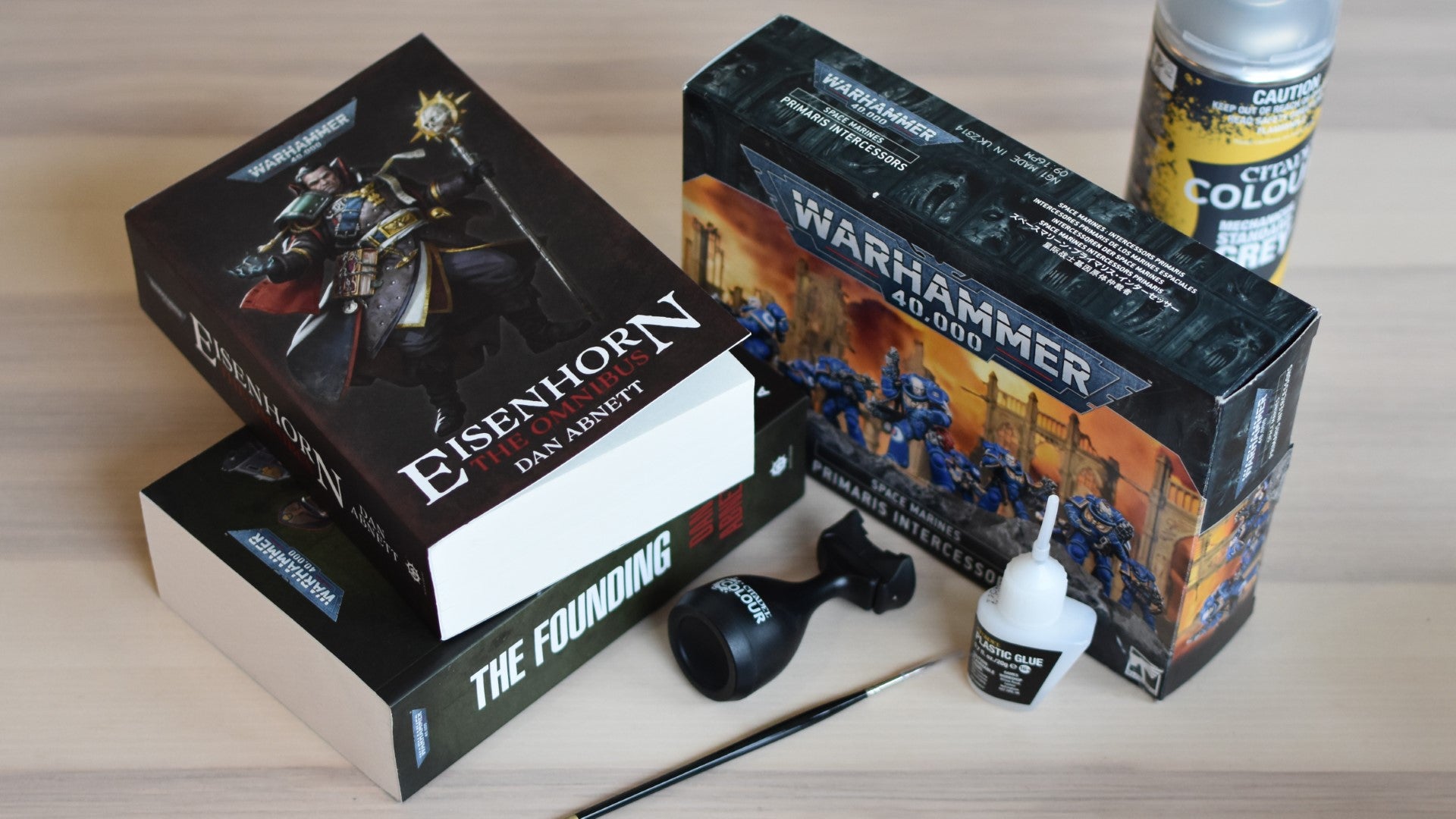 Two Warhammer 40,000 books next to a box of Space Marine miniatures and some painting equipment.