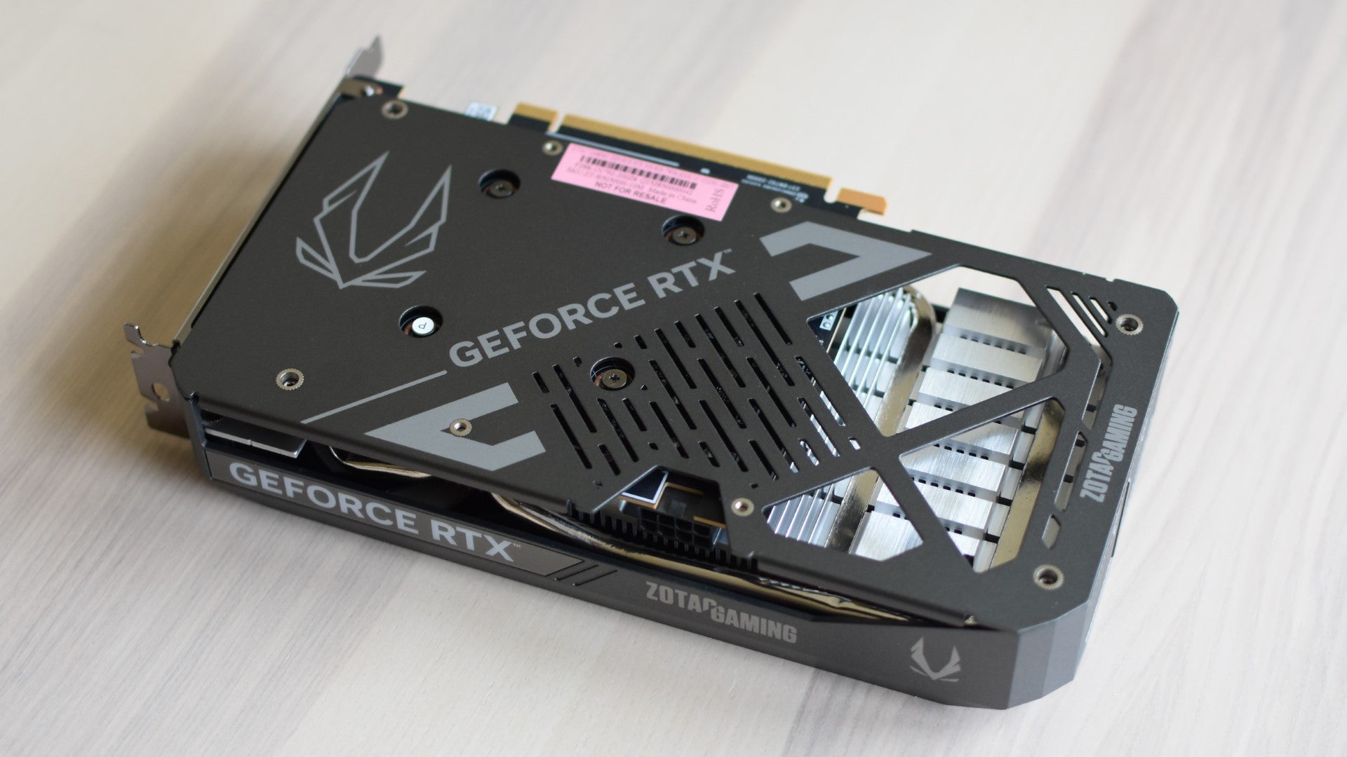 The Zotac Gaming GeForce RTX 5050 Twin Edge OC on a table, with its backplate side facing the camera. - 4