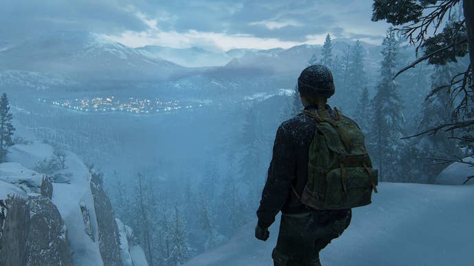 The Last of Us Part 2 character Abby looking from a high up snowy ledge at a settlement in the distance. They’re wrapped up warm and wear a beanie hat and carry a backpack.