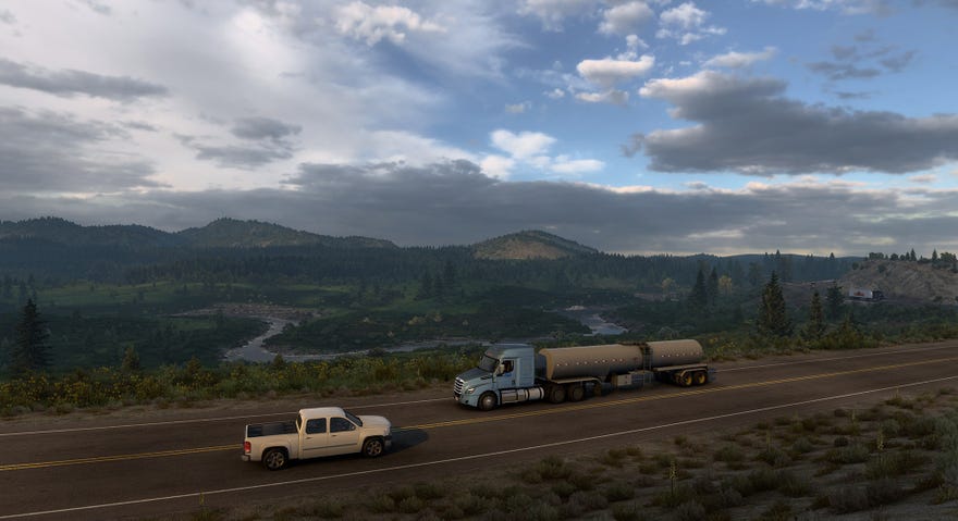 A screenshot of American Truck Simulator’s Wyoming DLC showing a truck driving on a road in front of a sprawling vista of river, mountains and trees.