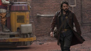 Cassian Andor walking in a still from Andor. A vehicle of some sort can be seen behind him, as well as a brick building.