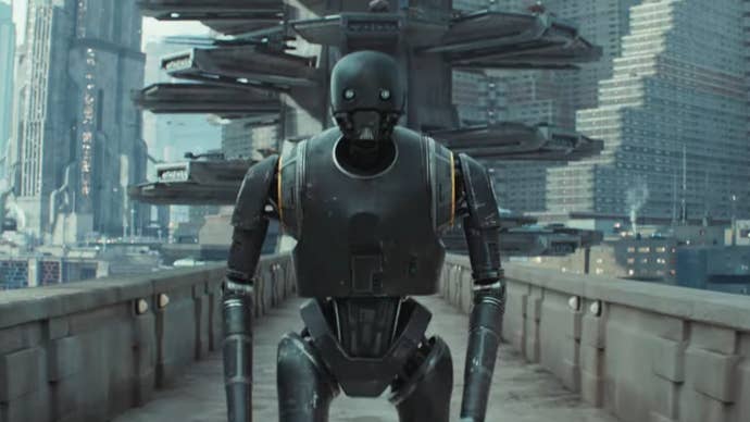 K-2SO, a large black human-shaped robot in Andor season 2, he is walking along a bridge, a sci-fi city in the background.
