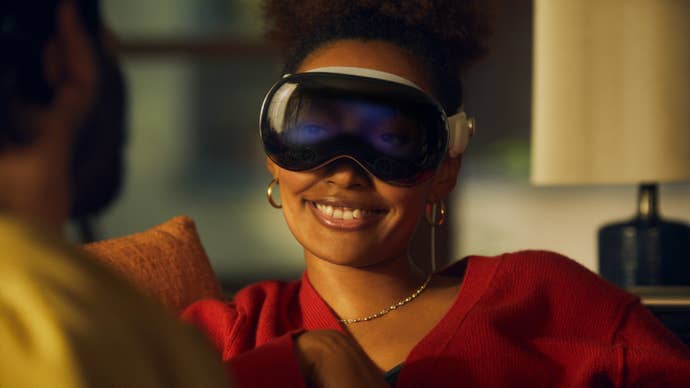 A woman wearing an Apple Vision Pro headset smiles as she looks toward another person