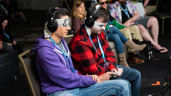 A promotional photo from Awesome Games Done Quick’s 2020 event showing two participants attempting a blindfolded speedrun together, both sharing a single controller at the same time.