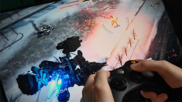 A player holds an Xbox Controller near a monitor screen playing Armored Core 6.