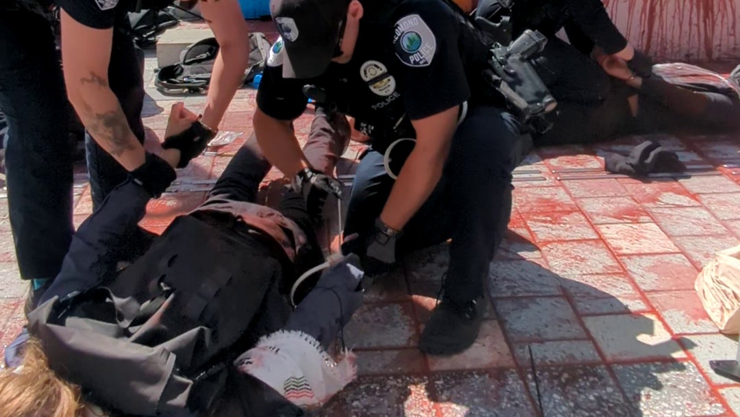 A close-up photograph of two pro-Palestinian protestors being arrested by police during a protest action at Microsoft's Redmond campus in August 2025. The protestors are lying on their faces while their arms are being restrained. - 10