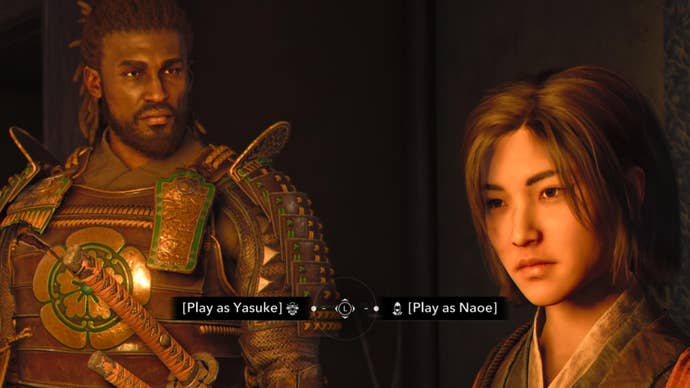 The two protagonists of Assassin’s Creed Shadows, Yaoe and Yasuke, stand together in a warmly lit room. Text at the bottom of the screen prompts the player to choose between the two characters.
