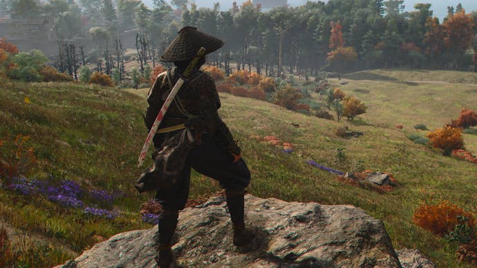 Naoe standing on a rock overlooking a green meadow while tracking the Kabukimono in Assassin’s Creed Shadows.