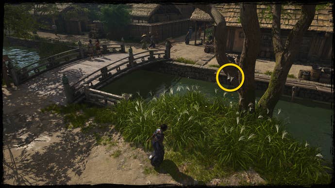 A close-up of a tree next to a bridge in Osaka in Assassin’s Creed Shadows, with a yellow circle highlighting the location of a white Origami Butterfly.