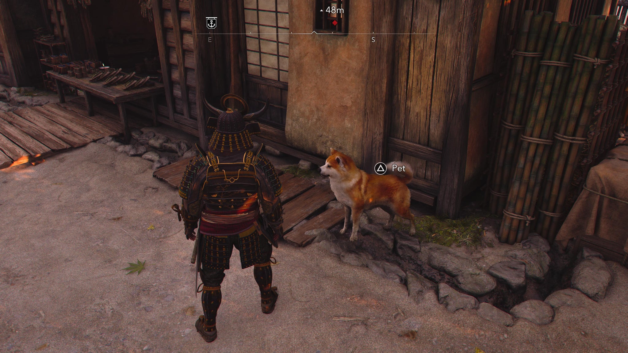An Assassin's Creed Shadows screenshot of Yasuke standing next to a dog outside a house; a prompt to pet is displayed above the dog's head. - 4