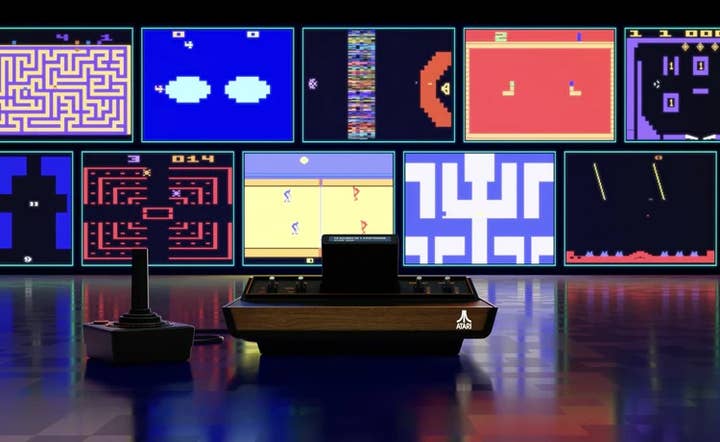 An image of the Atari 2600+ and a joystick sitting on a slightly reflective floor in the foreground. In the background is a wall of video screens showing Atari 2600 games