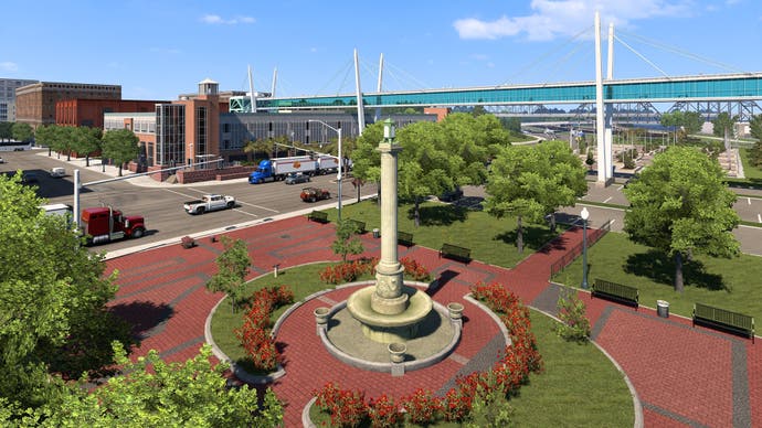 A screenshot of American Truck Simulator's Iowa expansion showing a column-like fountain in a city plaza surrounded by trees.